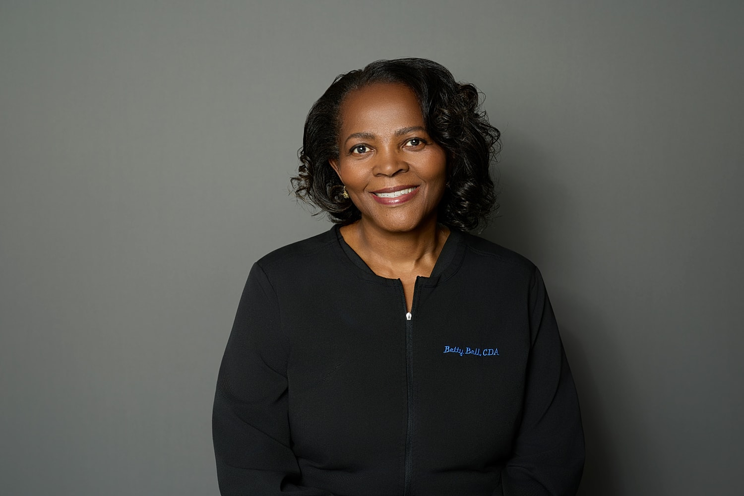 Smiling woman in professional attire against gray background.